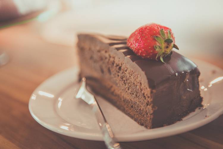 A slice of chocolate cake with a strawberry on top, sitting on a white plate A slice of chocolate cake with a strawberry on top, sitting on a white plate