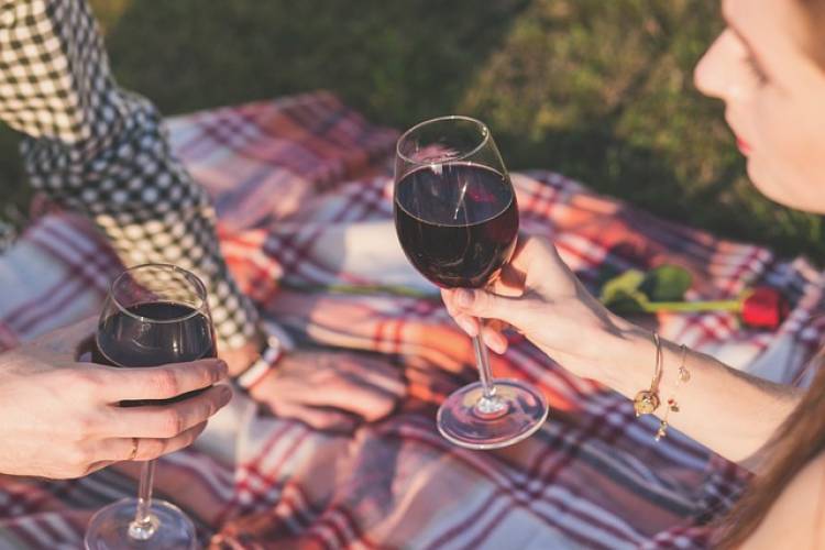 A couple shares two glasses of red wine on a picnic blanket A couple shares two glasses of red wine on a picnic blanket