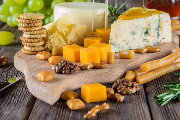 A large assortmemt of cheeses and crackers on a cutting board A large assortmemt of cheeses and crackers on a cutting board