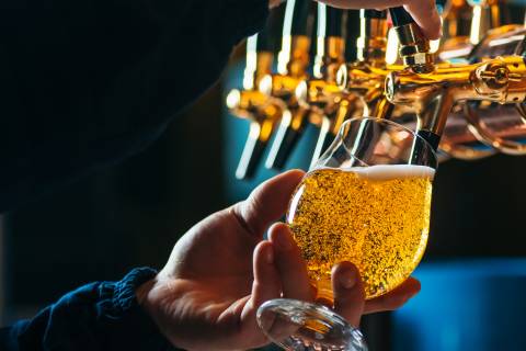 A hand holds a beer glass and pours a golden draught from a brass tap