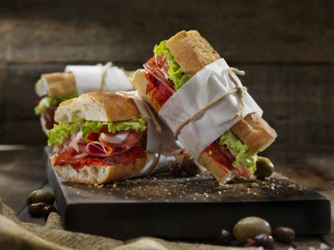 Sandwiches three six-inch italian subs. they are served on a long wooden board.