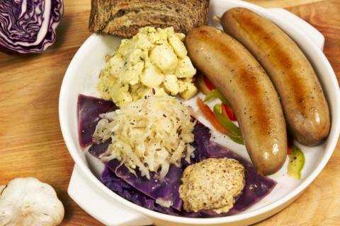 German Food sausage links served on plasticware with mustart, sauerkraut, and potato salad