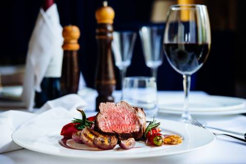 medium rate steak served atop grilled vegetables and a glass of red wine