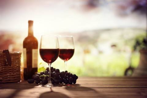 A pair of stemmed glasses with red wine stand on a table next to a bottle, all overlooking Texas Hill Country
